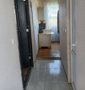 A narrow hallway leading to a small kitchenette with a window, a radiator, and a tiled floor.