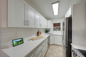 A modern kitchen with white cabinetry, a stainless steel refrigerator, and a built-in oven. - Bayside Bliss | First-Floor Condo with Water Views (St. Pete Beach)