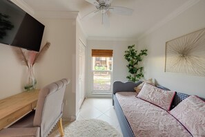 A room with a bed, a television, a ceiling fan, a window, and a plant. - Bayside Bliss | First-Floor Condo with Water Views (St. Pete Beach)