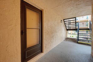A corridor with a closed door and a staircase leading to an outdoor area. - Bayside Bliss | First-Floor Condo with Water Views (St. Pete Beach)