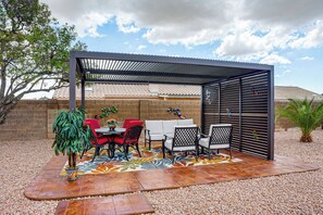 An outdoor patio with a covered seating area, a table with chairs, and decorative wall art. - Private Pool Oasis | Fiber Wi-Fi | Near Stadium (Peoria)