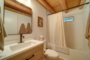 A bathroom with a wooden vanity, a toilet, a shower with a curtain, and a mirror with towels. - Cozy Prescott Cabin, Surrounded By Ponderosa Pines (Prescott)