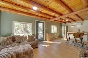 A spacious living area with a wooden ceiling, a sofa set, a dining table with chairs, and a kitchen area with an air conditioning unit. - Cozy Prescott Cabin, Surrounded By Ponderosa Pines (Prescott)