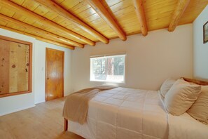 A bedroom with a wooden ceiling, a window, a bed with pillows, and a door. - Cozy Prescott Cabin, Surrounded By Ponderosa Pines (Prescott)