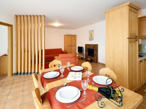 A dining area with a table set for four, a sofa, a TV, and wooden cabinets. - Aparthotel S-Bernardino SA, (San Bernardino), by Interhome (San  Bernardino)