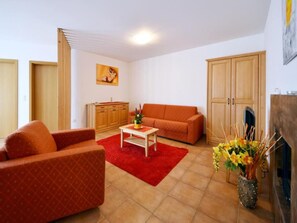 A living room with a sofa, a coffee table, and a red rug. There is a painting on the wall and a cabinet in the corner. - Aparthotel S-Bernardino SA, (San Bernardino), by Interhome (San  Bernardino)