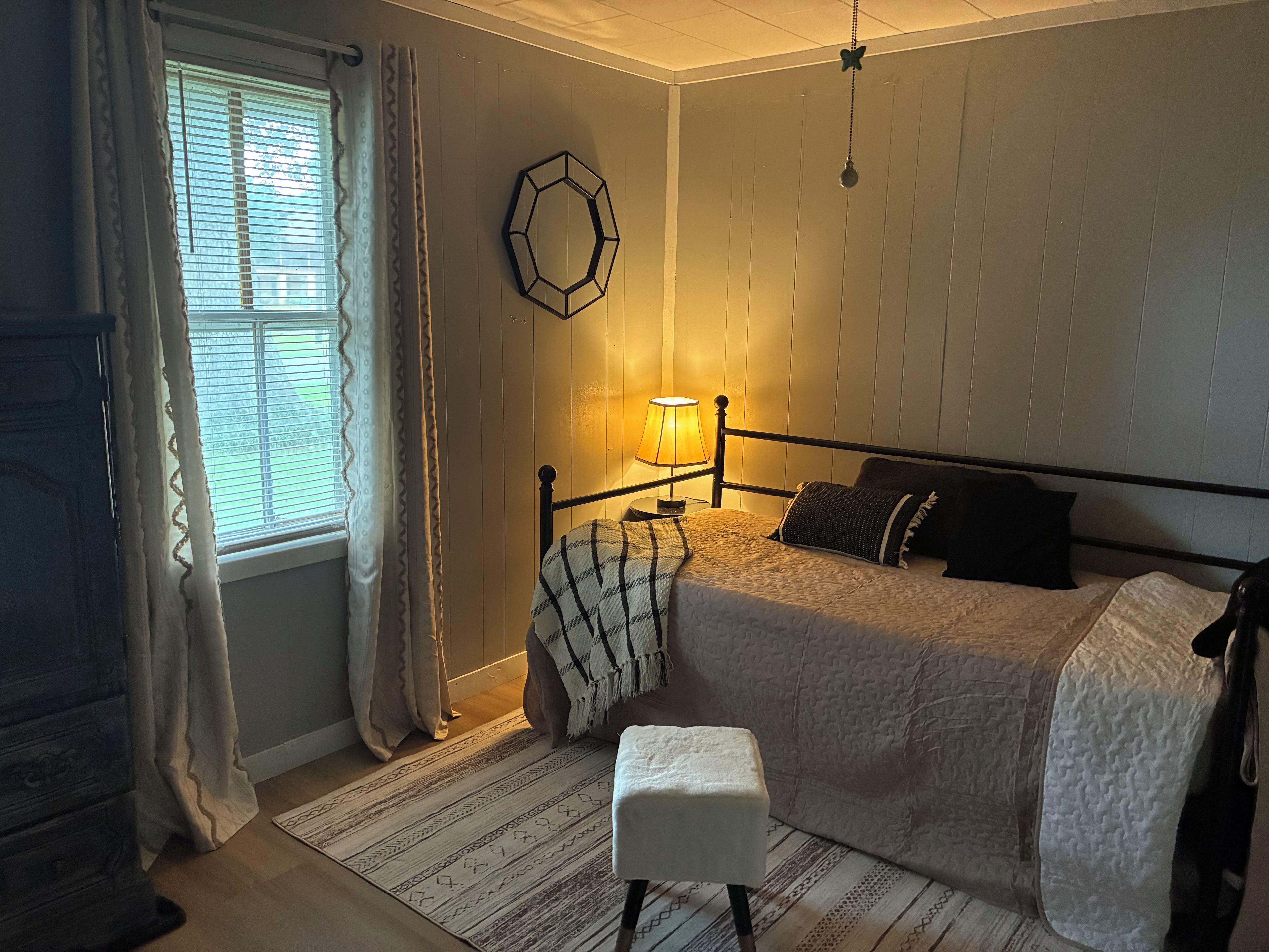 A bedroom with a bed, bedside lamp, and a window with curtains.