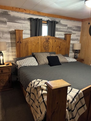 A bedroom with a wooden headboard, a bed with patterned bedding, two bedside tables with lamps, and a wooden nightstand.