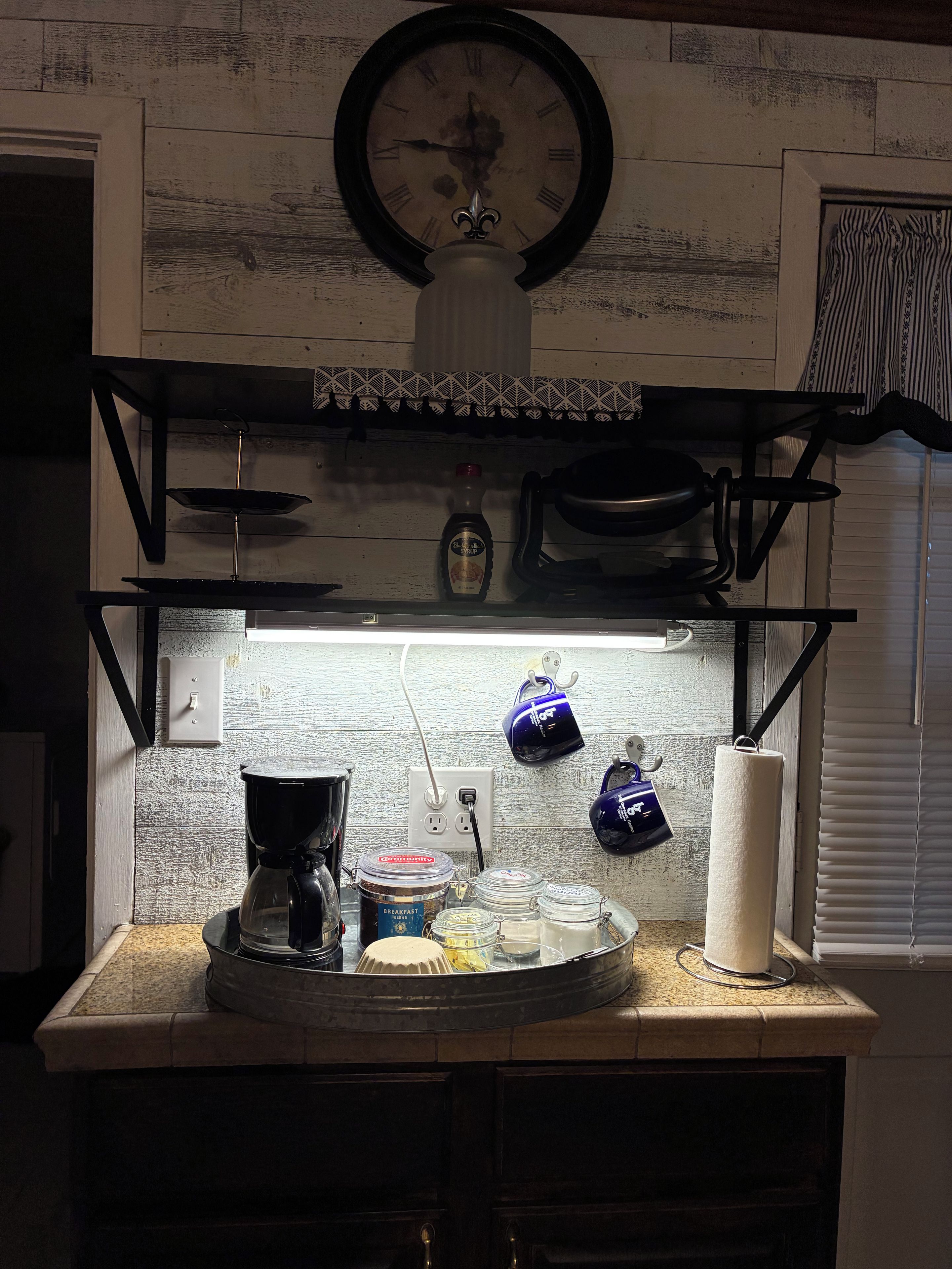 A kitchen with a clock, shelves, a coffee maker, jars, and a kettle.