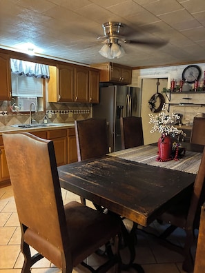 A kitchen with wooden cabinets, a stainless steel refrigerator, a dining table with a placemat, and a ceiling fan. - 3-bedroom house within walking distance to shopping, eats , church, schools (Kaplan)