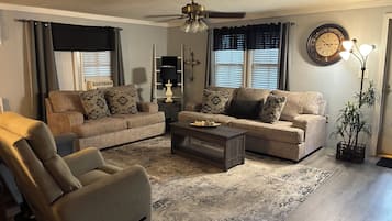 A living room with a sofa, armchair, coffee table, and a potted plant.