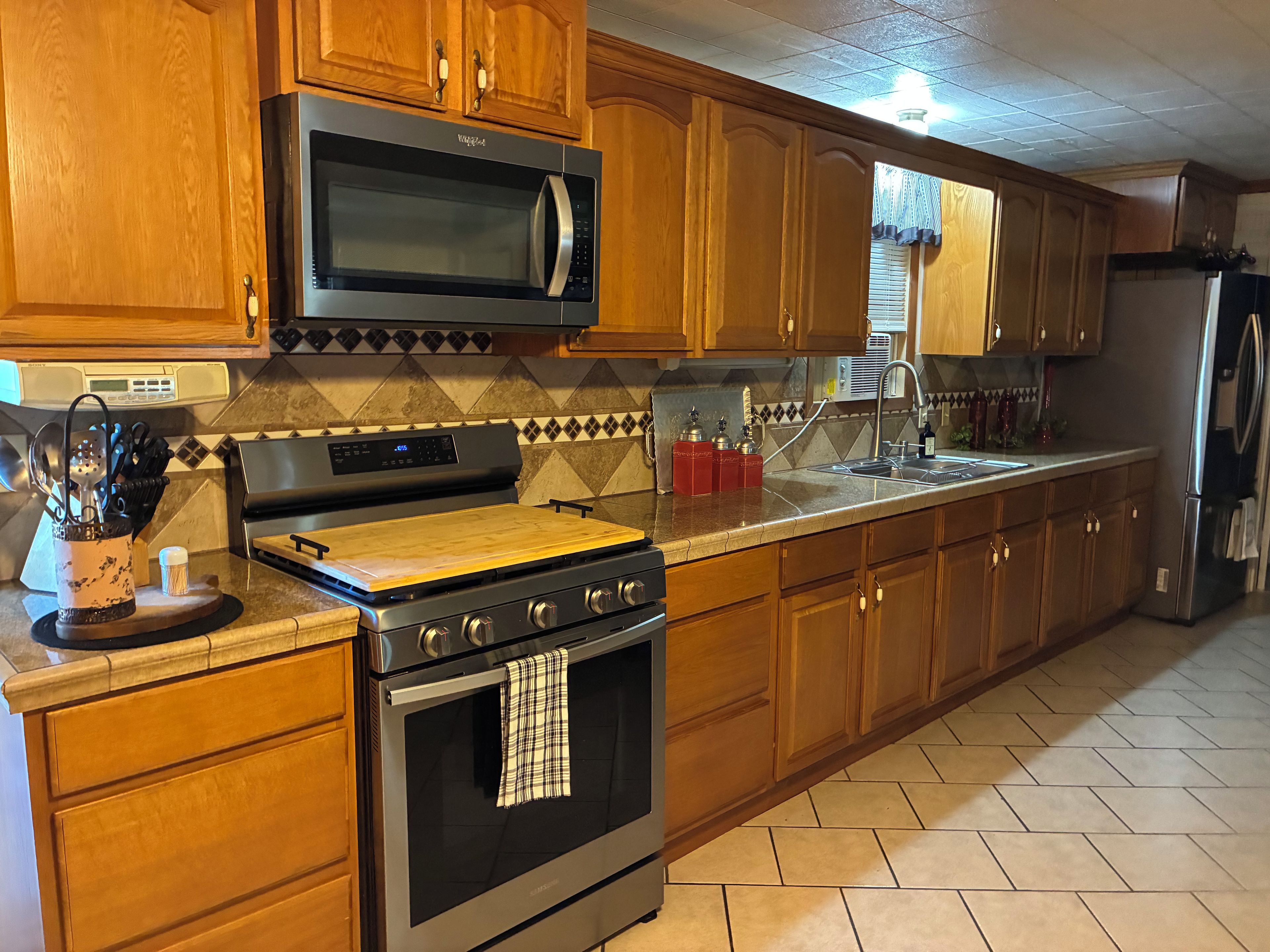 A kitchen with wooden cabinets, a stainless steel microwave, a gas stove, and a refrigerator.