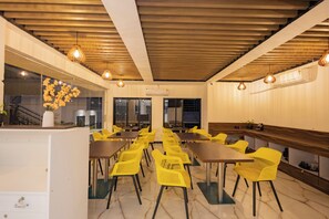 A dining area with yellow chairs and tables, wooden ceiling beams, and hanging pendant lights.