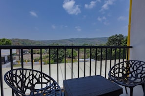 A balcony with two chairs and a table, overlooking a hilly landscape.