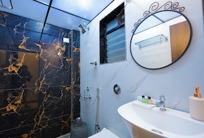A bathroom with a black and gold marble shower wall, a round mirror, a sink with toiletries, and a window with a metal grill. - Coastal Cliff by ILIF Hotels (Murud)