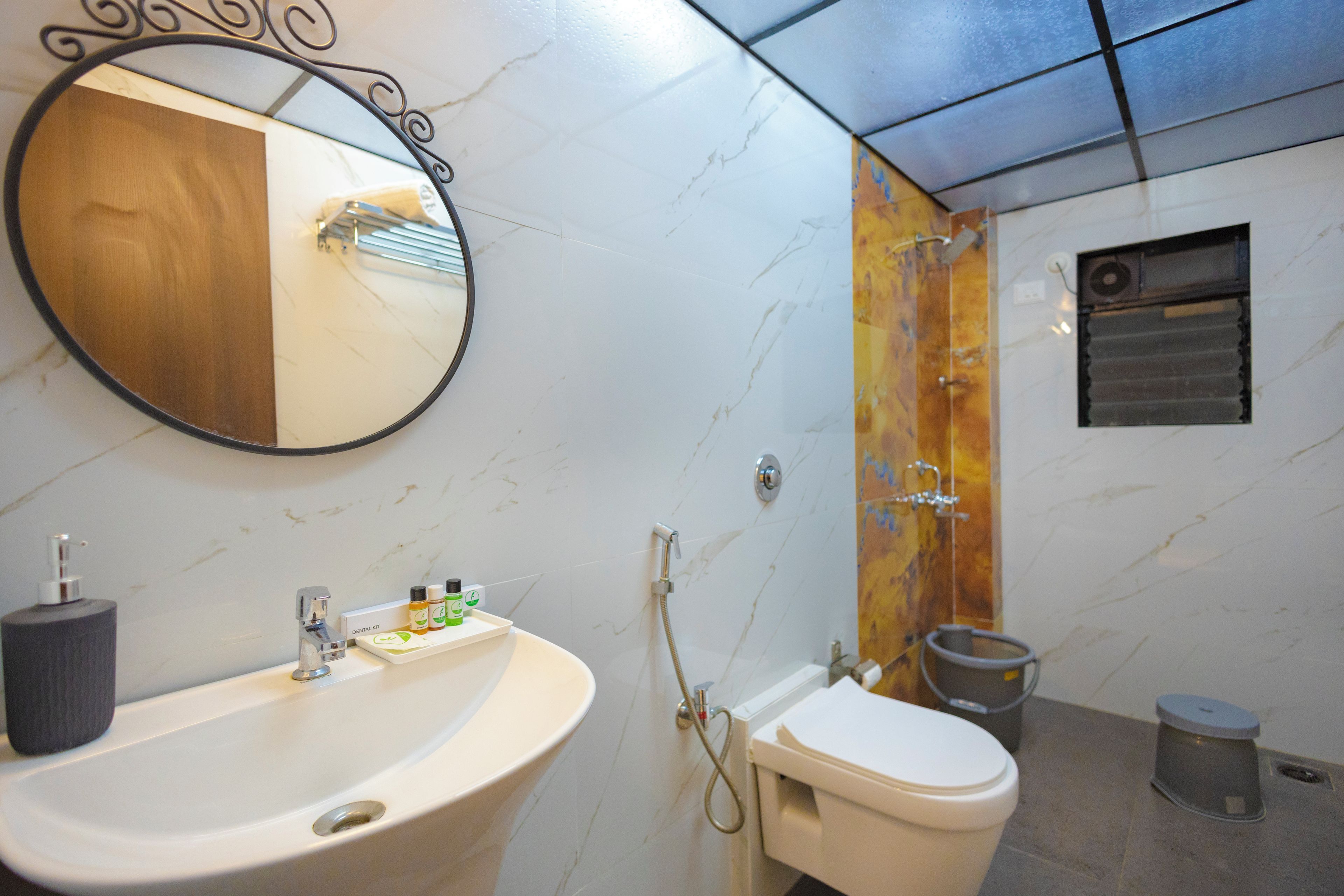 Un baño con pared de mármol, lavamanos, inodoro, ducha y espejo.