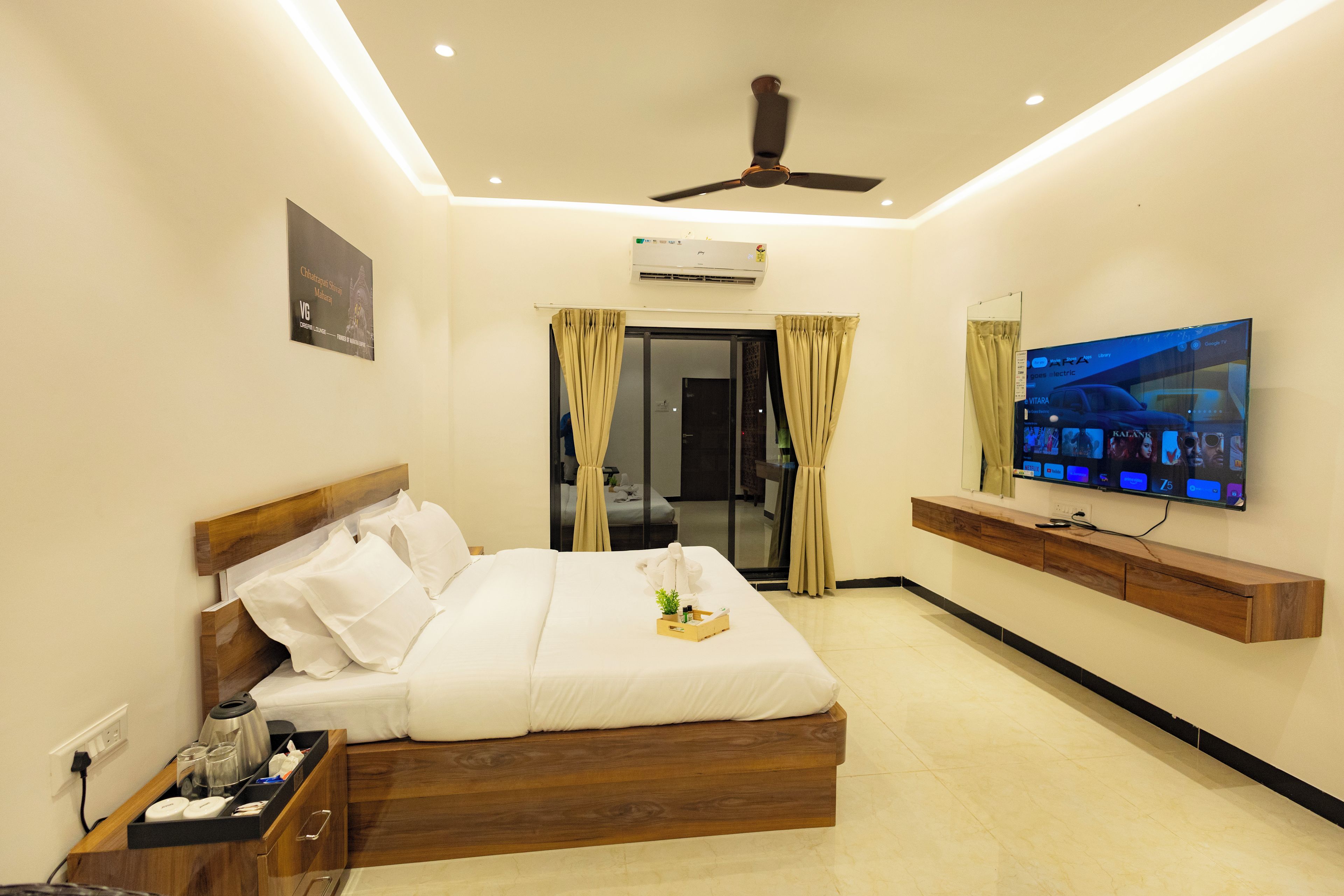 Habitación de hotel con cama, televisión, ventilador de techo y ventana con cortinas.