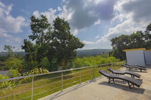 A terrace with lounge chairs and a view of a lush landscape.
