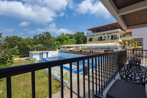 A balcony with a view of a pool and a building with a yellow and white facade.