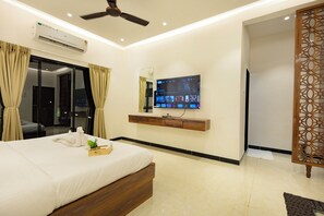 A hotel room with a bed, a TV mounted on the wall, a ceiling fan, and an air conditioning unit.