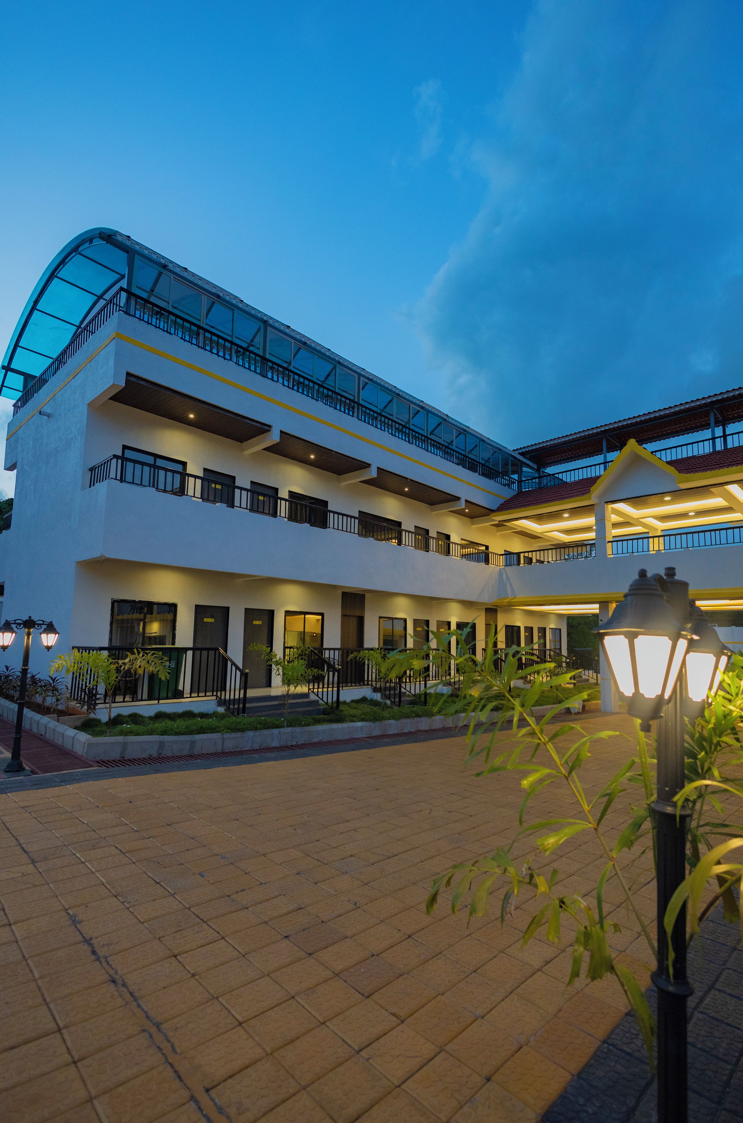 A multi-story hotel with a glass facade, outdoor lighting, and a paved courtyard.