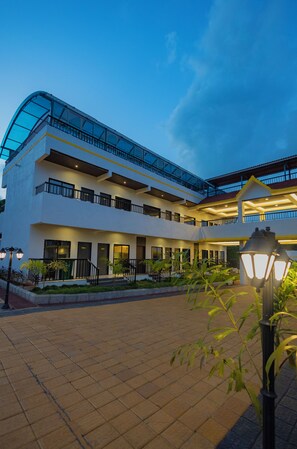 A multi-story hotel with a glass facade, outdoor lighting, and a paved courtyard.