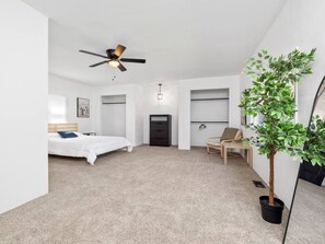 Quarto com cama, ventilador de teto, planta em vaso e uma cadeira.