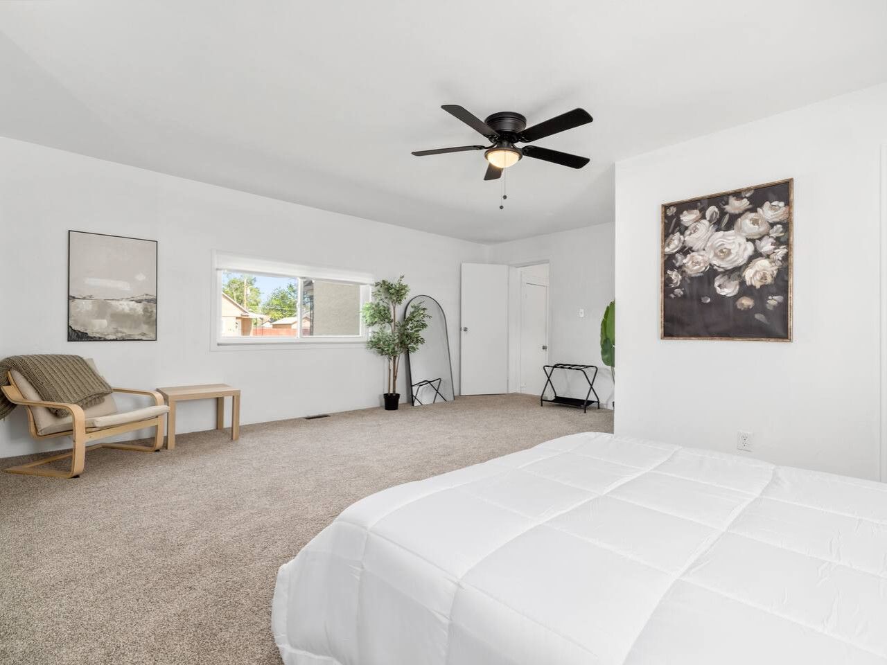 A bedroom with a bed, a ceiling fan, a window, a chair, and a plant.