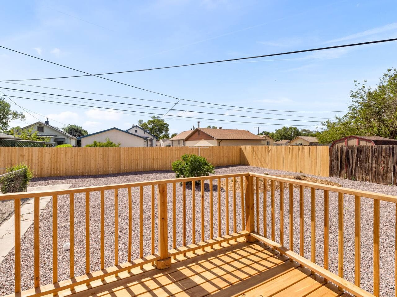 Une terrasse en bois avec une rambarde en métal, entourée d’une zone recouverte de gravier et d’une clôture en bois.