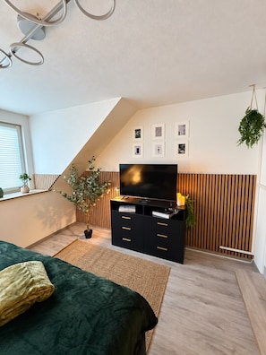 Una camera da letto moderna con soffitto spiovente, un mobile porta TV nero, un letto verde e una pianta in vaso.