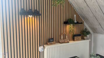Ein Zimmer mit einer horizontalen Holzwand, einem weißen Heizkörper, einem schwarzen Tisch mit einer gewebten Tischunterlage und einer hängenden Pflanze.