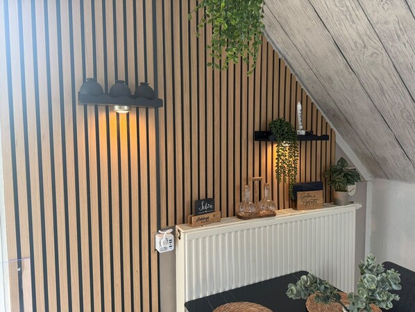 A room with a slatted wooden wall, a white radiator, a black table with a woven placemat, and a hanging plant.