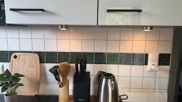 Een keuken met witte kasten, een snijplank, een messenhouder, een waterkoker en een potplant.