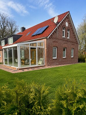 A two-story brick house with a red-tiled roof, a glass-enclosed patio, and a well-maintained lawn.