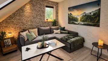 Ein gemütliches Wohnzimmer mit Steinwand, einem Ecksofa, einem Couchtisch und einem Landschaftsbild.