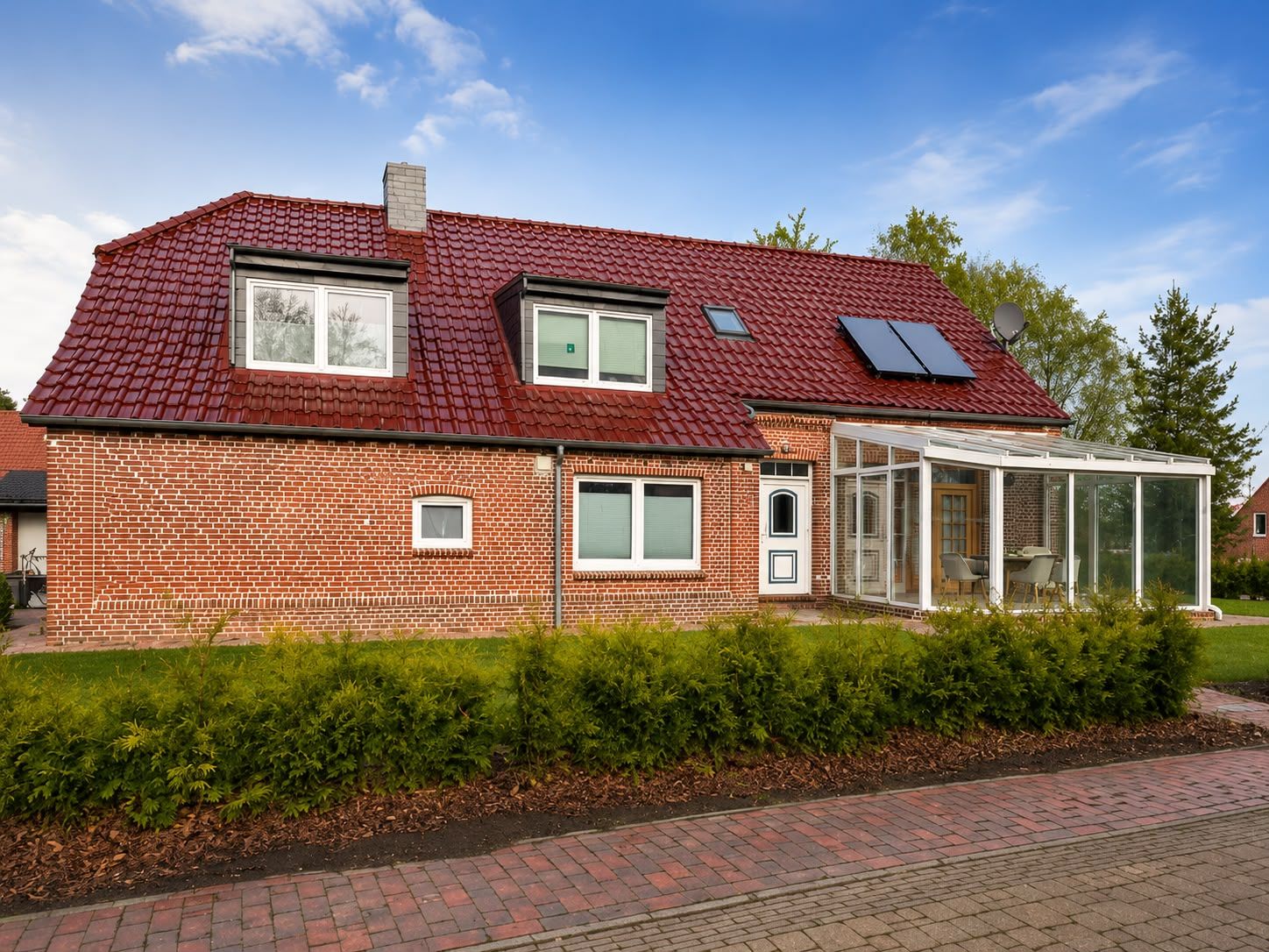 Ein Ziegelhaus mit rotem Ziegeldach, einem Wintergarten und einem gepflegten Garten.