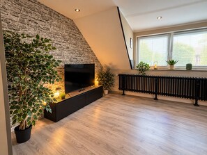A modern living room with a stone wall, a black entertainment unit, a large TV, and a radiator.