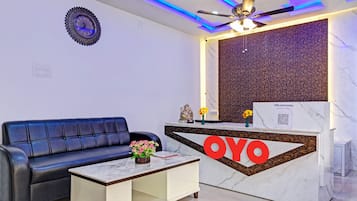 Ein Empfangsbereich mit einer Couch, einem Couchtisch, einem Empfangsschalter mit dem Schild 'OYO' sowie einem Deckenventilator und einer Wanddekoration.