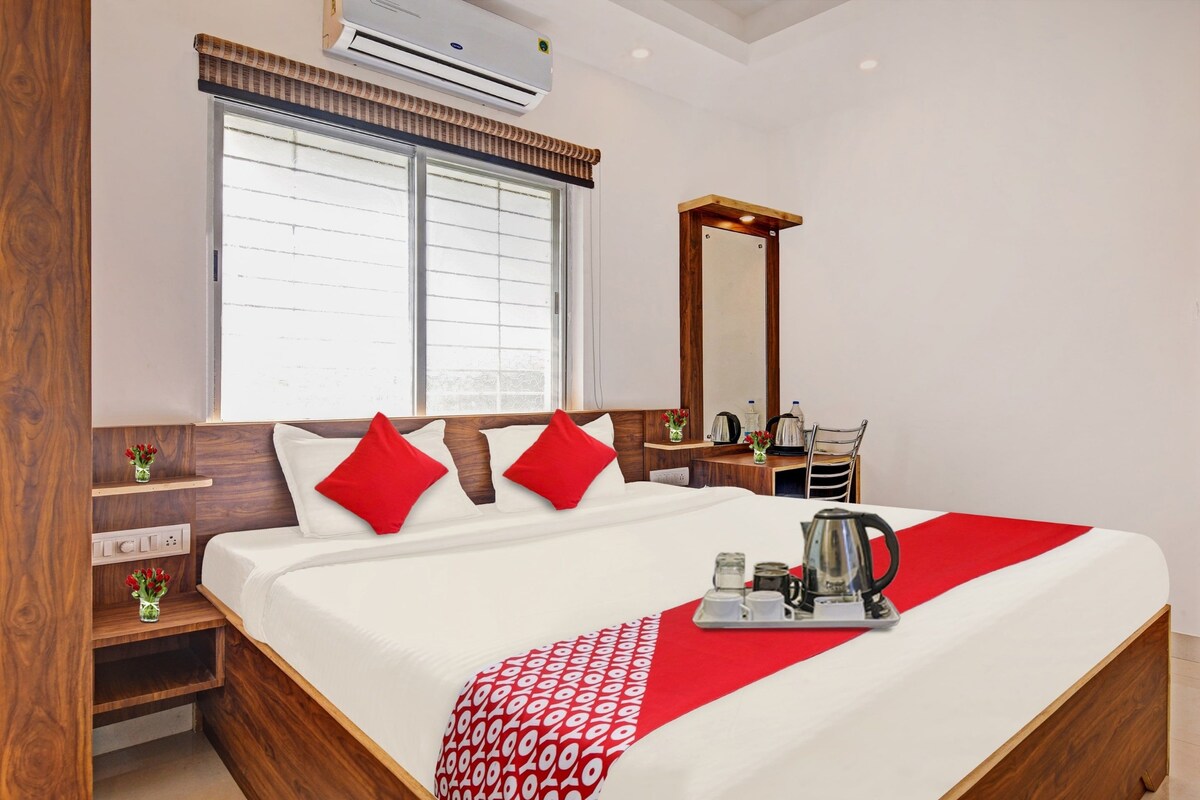 A hotel room with a bed, a nightstand, a mirror, and a window with blinds.