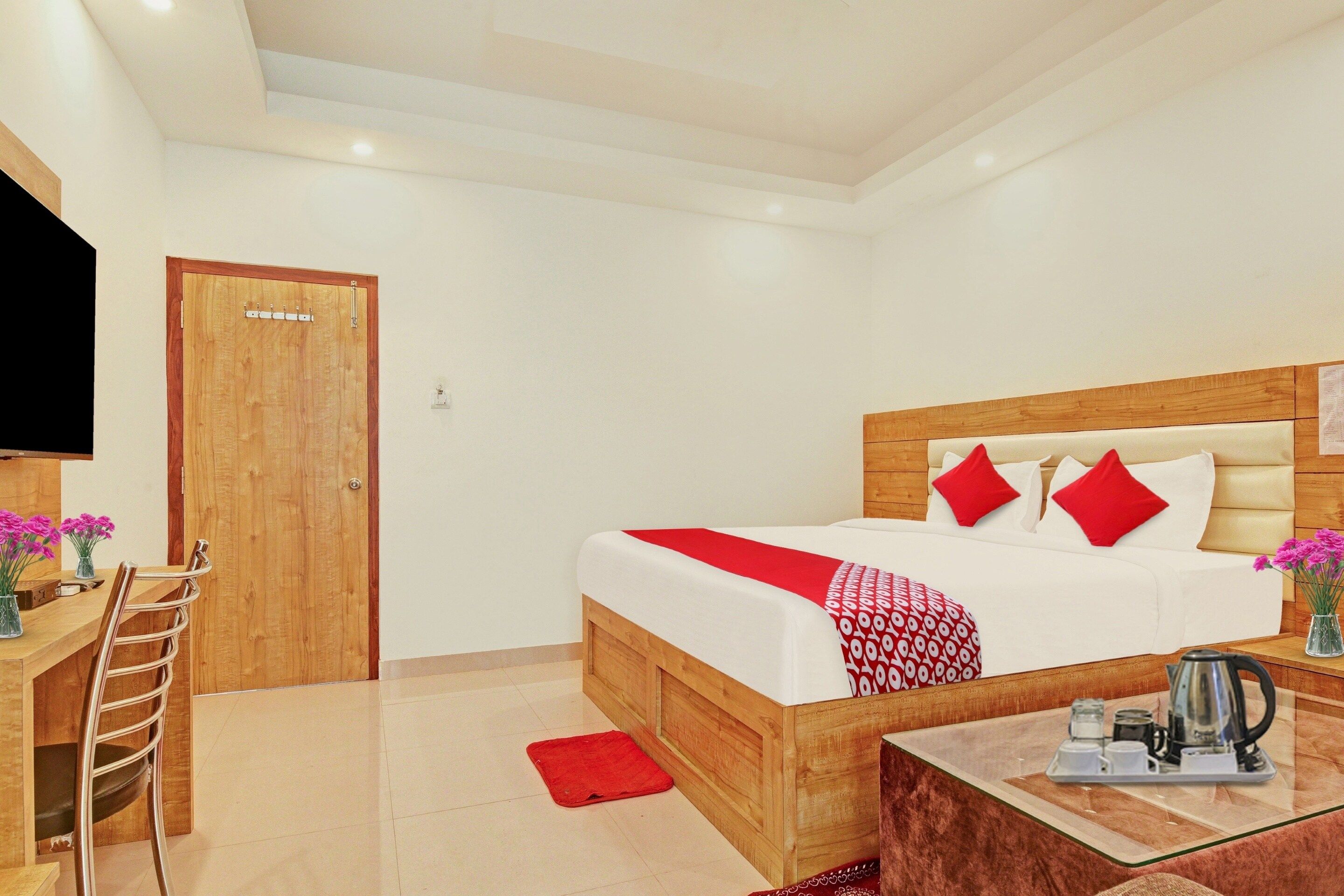 A hotel room with a wooden bed, a desk with a chair, a television, and a coffee table with a kettle.