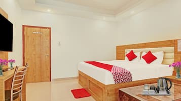 A hotel room with a wooden bed, a desk with a chair, a television, and a coffee table with a kettle.