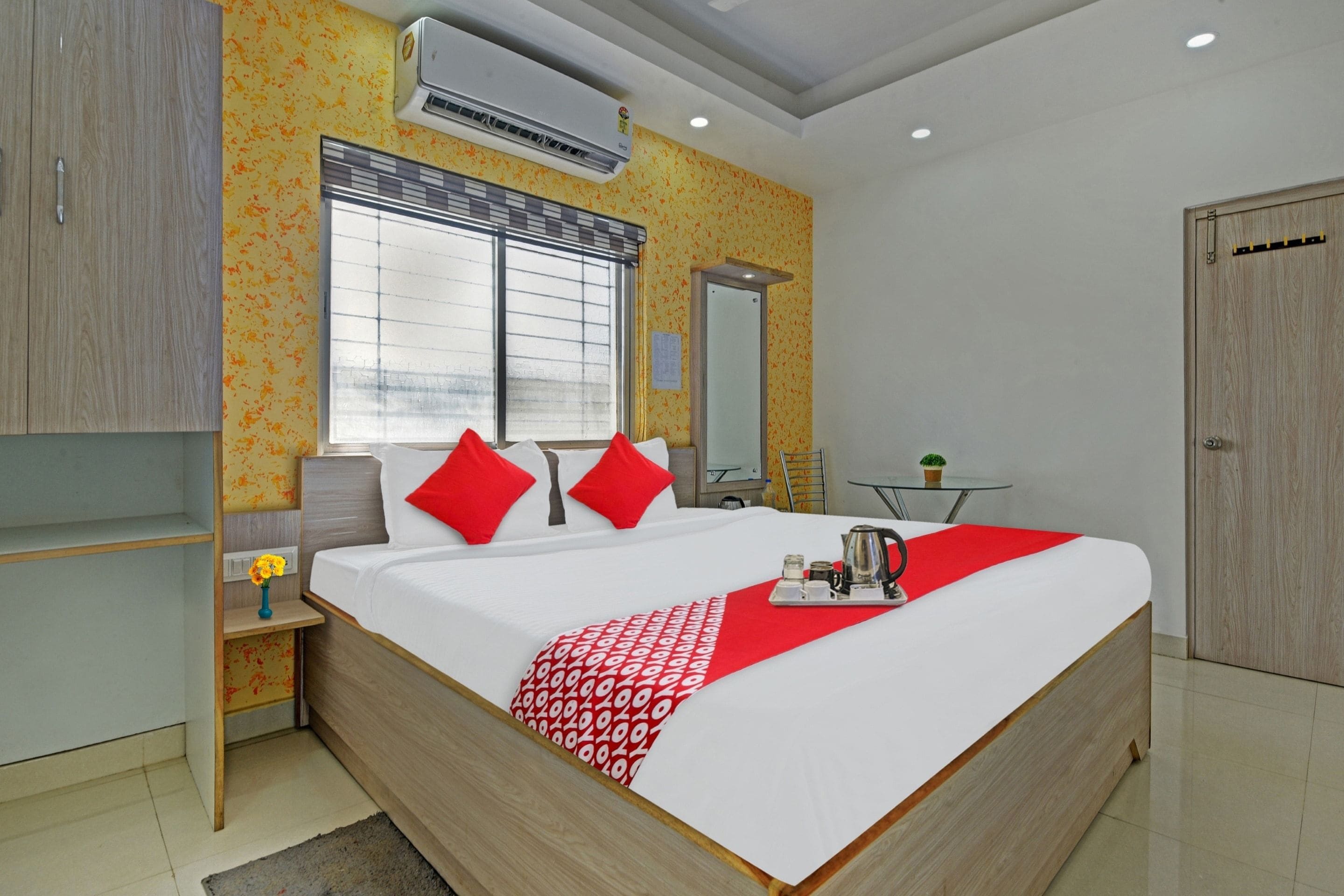 A modern hotel room with a large bed, a bedside table, a small table with a plant, and a wardrobe.