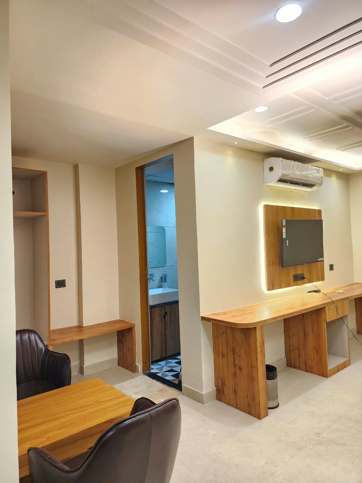 Une chambre moderne avec un bureau en bois, une télévision et une salle de bain visible à travers une porte ouverte.