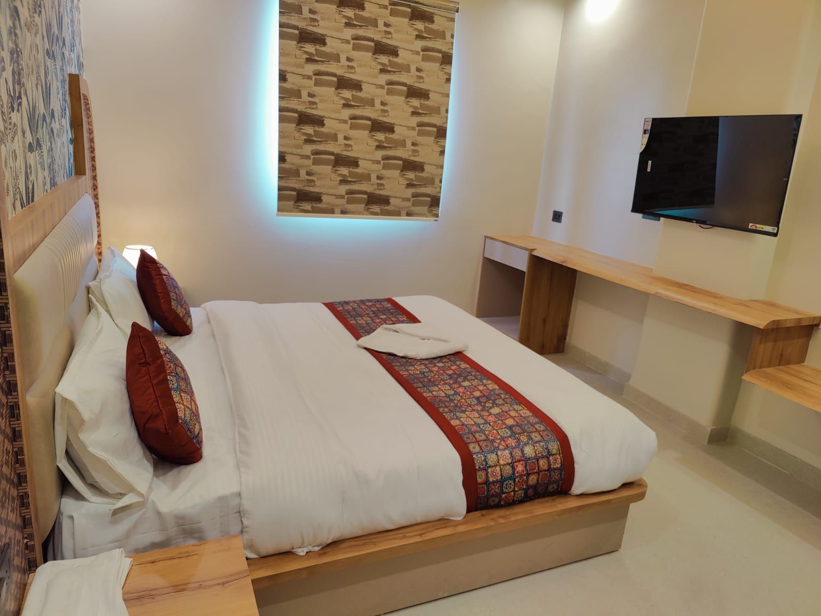 Une chambre d’hôtel avec un lit, une télévision, un banc en bois et un mur orné d’un motif.