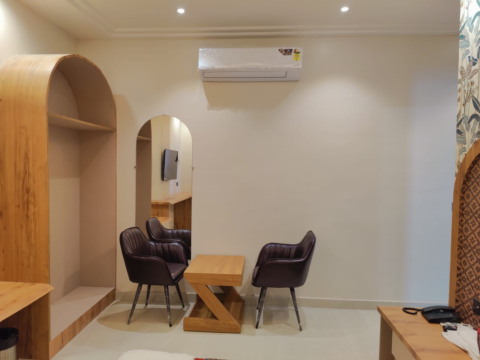 Une petite pièce moderne, dotée d’un bureau en bois, de deux fauteuils en cuir, d’une table en bois, d’un téléviseur à écran plat fixé au mur et d’un climatiseur mural.
