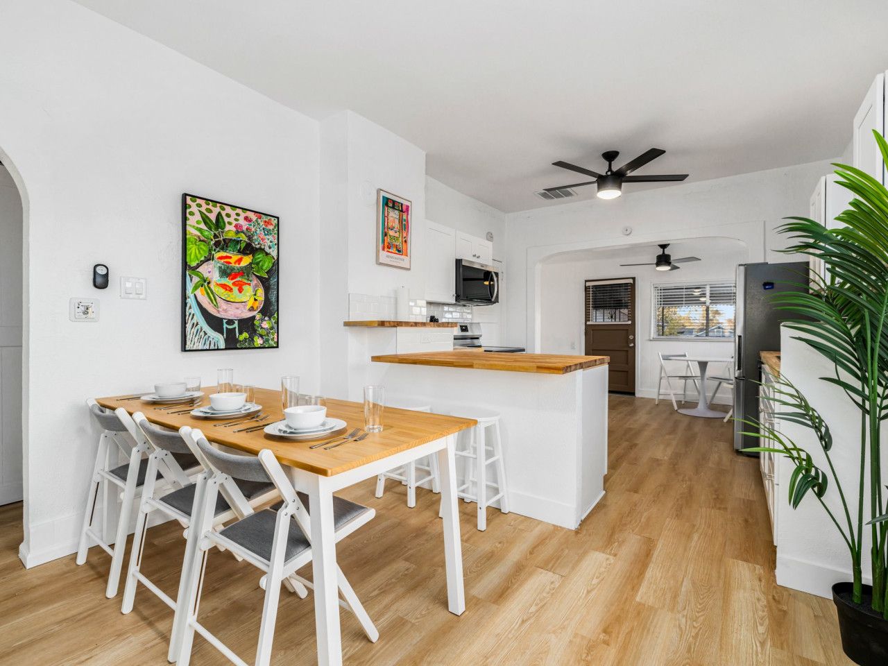 Una cocina moderna con armarios blancos, una isla de madera y un comedor con sillas blancas.