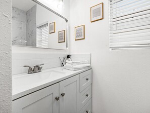 A bathroom with a white sink, mirror, and framed pictures on the wall. - Casitas en Pueblo - Washington House (Pueblo)