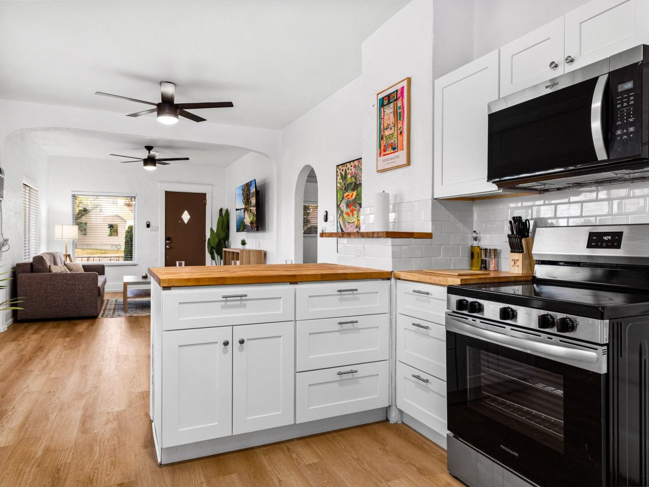 Une cuisine moderne avec des meubles blancs, une cuisinière noire et un four à micro-ondes. On y trouve un plan de travail en bois et un ventilateur de plafond.