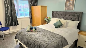 Een slaapkamer met een bed, een stoel, een kledingkast en een raam met gordijnen.