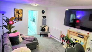 Ein Wohnzimmer mit grauem Sofa, Fernseher, Pflanze und kleinem Tisch mit einem Schild.